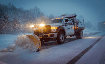 A truck plowing snow during a heavy snowstorm.